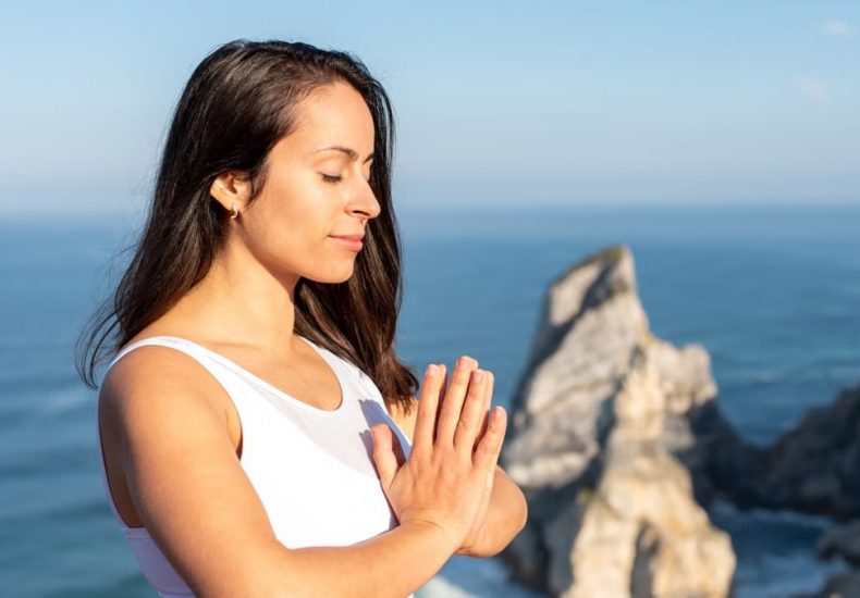 A woman meditates peacefully by the ocean in Portugal, embracing wellness.